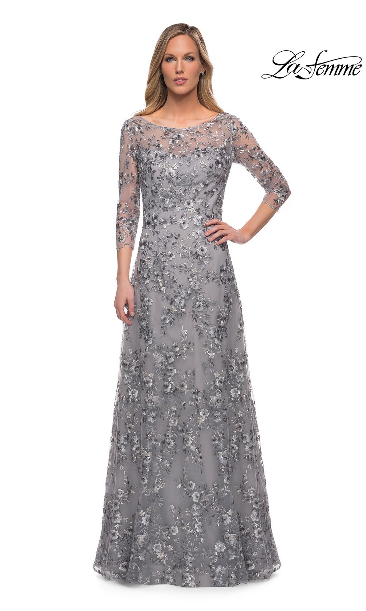 Woman in Long Formal Dress: La Femme 29903—silver, floor-length, with metallic floral lace embroidery—stands against a white background. “La Femme” logo top right.